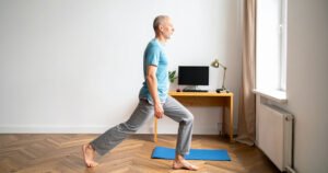 A middle-aged man doing a lunge beside his desk at home